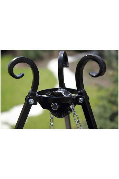 Nahaufnahme eines schwarzen Metallstativs mit eingerollten Haken und Ketten im Freien vor einem unscharfen grasbewachsenen Hintergrund.