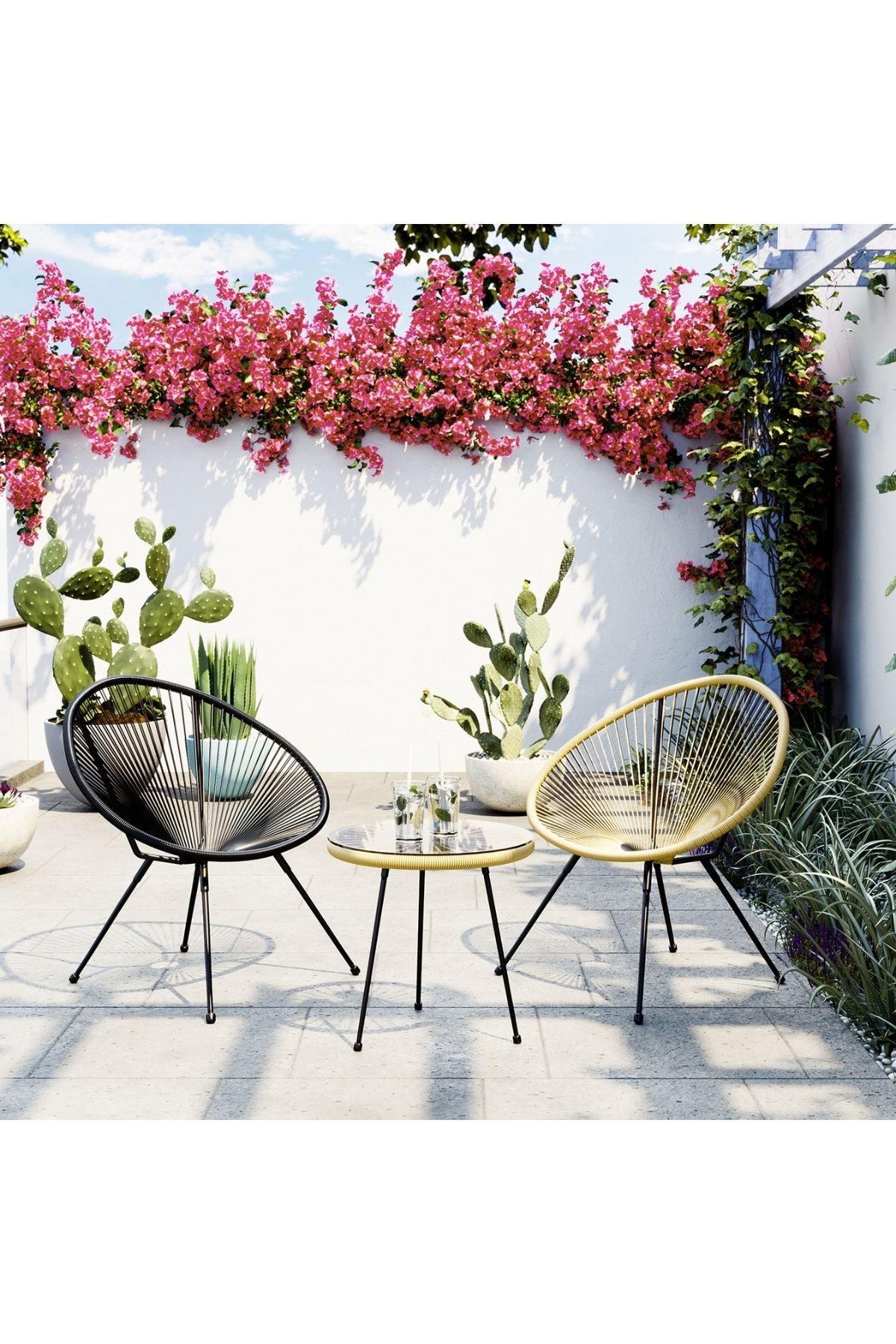 Zwei moderne Stühle und ein kleiner runder Tisch stehen auf einer Terrasse mit Kakteen und blühenden Pflanzen vor einer weißen Wand im Hintergrund.