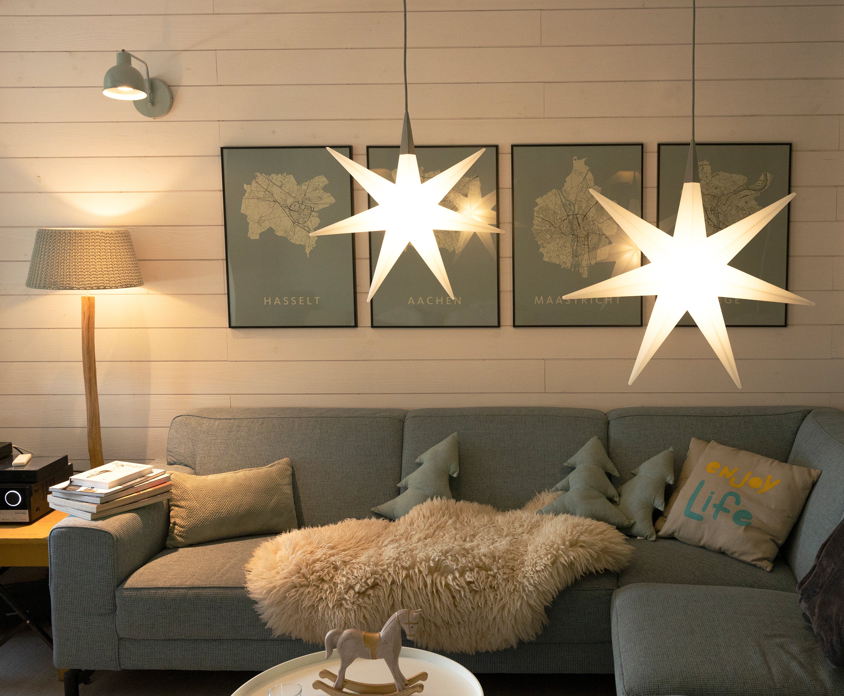 Gemütliches Wohnzimmer mit sternförmigen Pendelleuchten, einem blauen Sofa und Landkarten an der Wand.