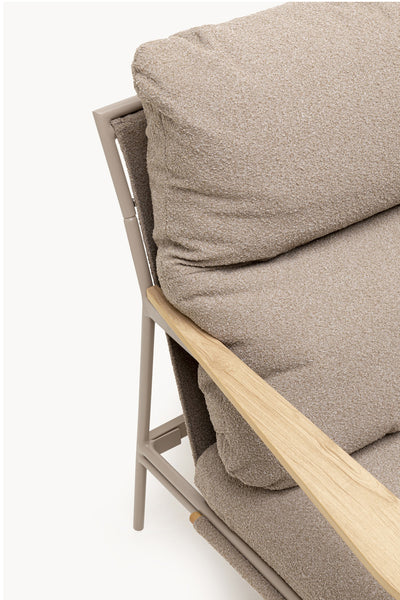 Nahaufnahme eines gepolsterten Stuhls mit Armlehne aus hellem Holz und beigefarbenem, strukturiertem Bezug vor einfarbigem Hintergrund.