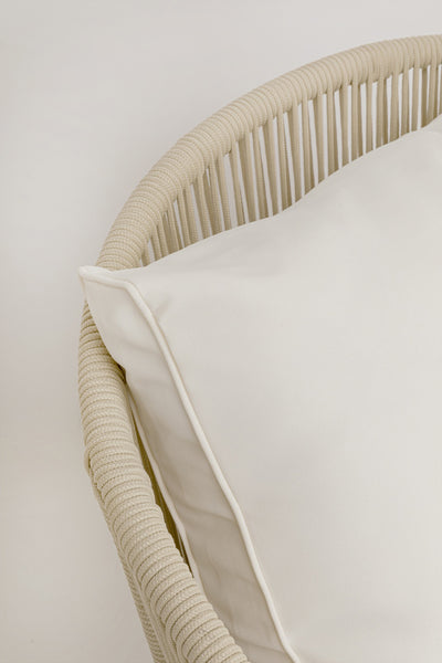 Nahaufnahme eines beigefarbenen geflochtenen Stuhls mit einem großen, cremefarbenen Kissen.