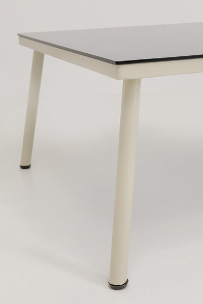 Nahaufnahme eines Tisches mit schwarzer Platte und weißen Metallbeinen vor einem schlichten weißen Hintergrund.