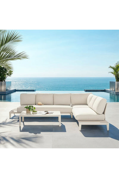 Modernes Terrassenset mit beigem Sektionssofa und Couchtisch auf einer Terrasse mit Blick auf den ruhigen Ozean, mit Palmen auf jeder Seite.