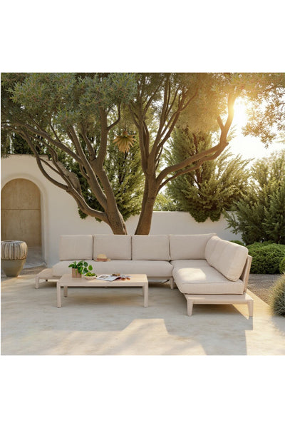 Ein beiges Outdoor-Sofa mit passendem Couchtisch steht auf einer Terrasse unter einem großen Baum, umgeben von Grün und sanftem Sonnenlicht.