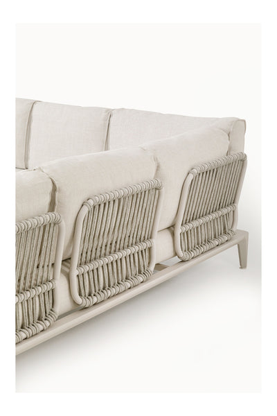 Helles Sofa mit Plüschkissen und einer sichtbaren Rückenlehne mit geflochtenem Seilmuster auf einem Metallrahmen vor einem schlichten weißen Hintergrund.