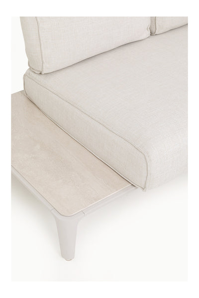 Nahaufnahme eines hellbeigen gepolsterten Sofas mit einem integrierten hellen Beistelltisch aus Holz oder Stein an einem Ende.