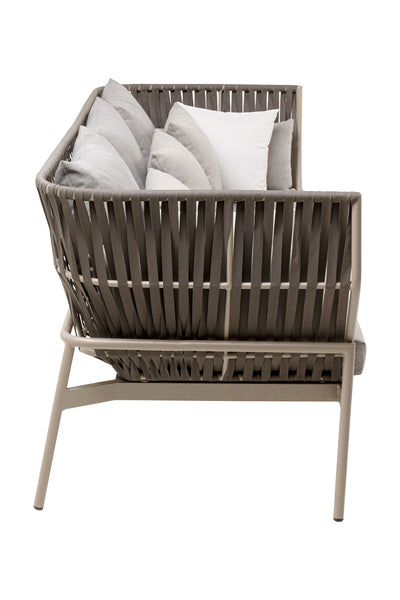 Ein moderner Stuhl für den Außenbereich mit geflochtener Rückenlehne und Sitzfläche, mit mehreren grauen und weißen Kissen.