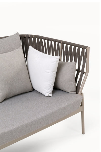 Modernes Outdoor-Sofa mit taupefarbenem Gestell, geflochtener Rückenlehne und drei Kissen - zwei graue und ein weißes - vor einem schlichten weißen Hintergrund.