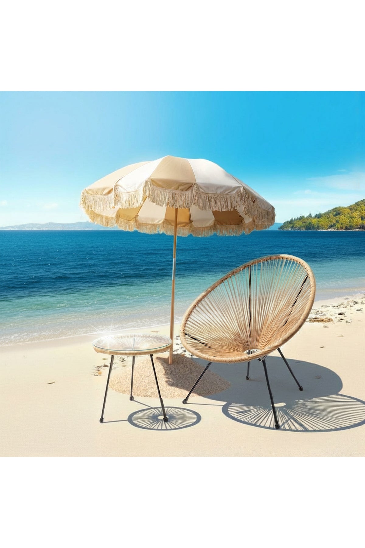 Ein runder Korbstuhl und ein kleiner Tisch stehen unter einem fransenbesetzten Sonnenschirm am Sandstrand mit blauem Meer und klarem Himmel im Hintergrund.