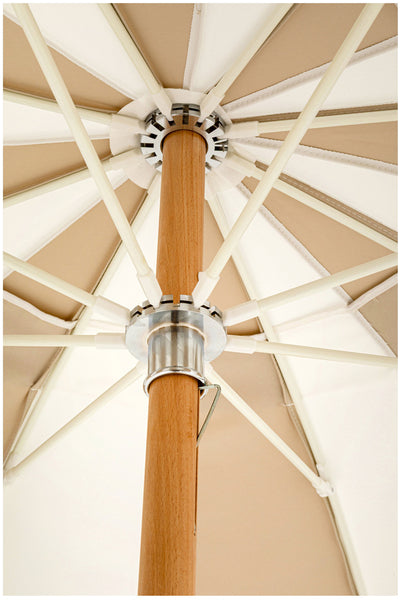 Nahaufnahme der Unterseite eines beigen Terrassenschirms, die den Holzmast, die Metallverbindung und die radialen Stützrippen zeigt.