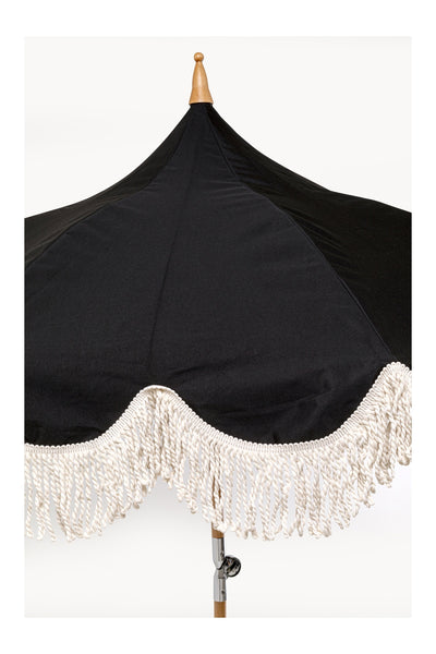 Ein schwarzer Regenschirm für den Außenbereich mit einem hölzernen Endstück und weißen Fransen am Rand.