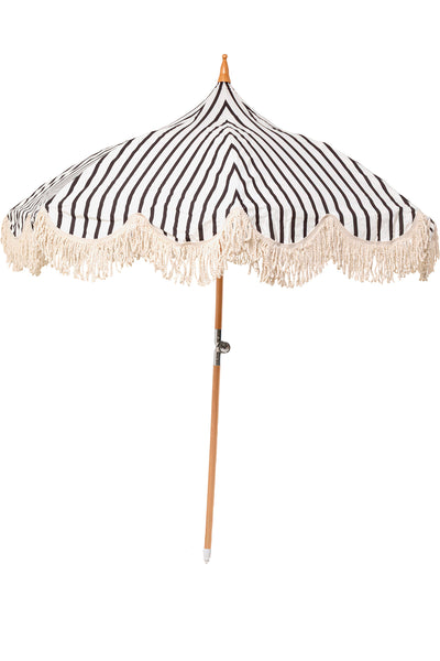 Ein Sonnenschirm mit schwarzen und weißen vertikalen Streifen und ausgefransten Rändern, der von einer Holzstange getragen wird, ist vor einem weißen Hintergrund abgebildet.