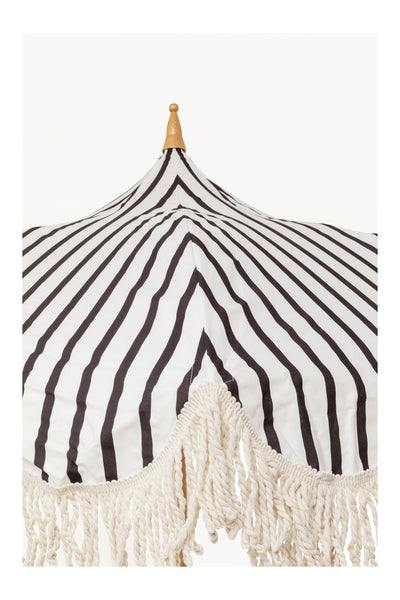 Schwarz-weiß gestreifter Regenschirm mit spitzer Holzspitze und Fransenbesatz am Rand.