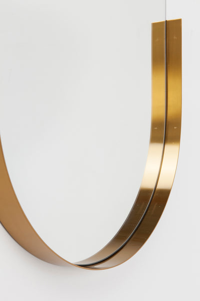 Eine Nahaufnahme eines modernen, goldenen Metallrahmens, der sich vor einem weißen Hintergrund nach oben wölbt.