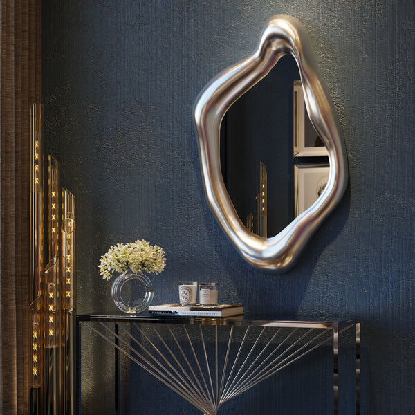 Abstrakter Silberspiegel über einem modernen Konsolentisch mit Blumen und Kerzen vor einer dunkel strukturierten Wand.