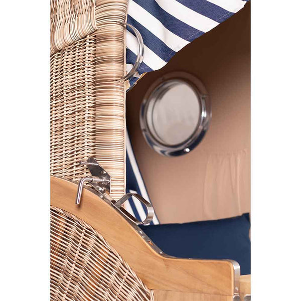 Nahaufnahme eines Korbstuhls mit einem gestreiften Stoffdach, einer Metallspange und einem kleinen runden Fenster im Hintergrund.