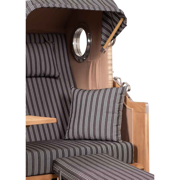 Nahaufnahme eines hölzernen Strandstuhls mit schwarz-weiß gestreiften Polstern, einem passenden Kissen, einem kleinen runden Fenster und einem ausklappbaren Tablett an der Armlehne.