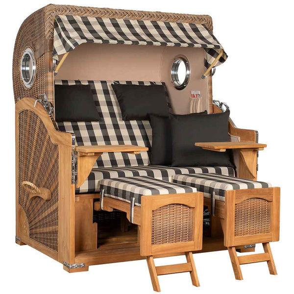 Ein Strandkorb mit Baldachin, karierten Kissen, zwei Fußstützen, zwei Seitentabletts und schwarzen Wurfkissen.