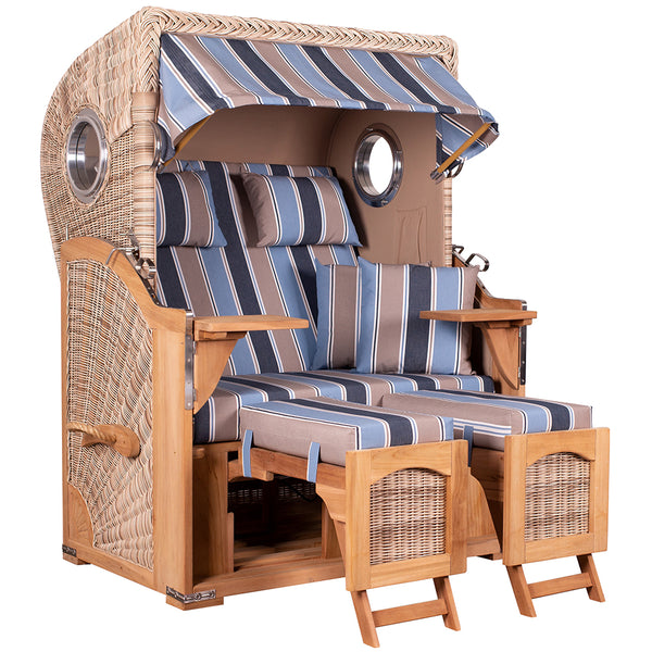 Ein Strandkorb mit Baldachin, gepolsterten Kissen, blau braun weiß gestreiften Kissen, Armlehnen aus Holz, ausklappbaren Fußstützen und Bullaugen an den Seiten.