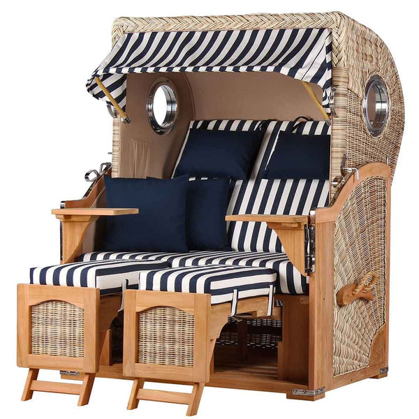 Ein Strandkorb für zwei Personen mit blau-weiß gestreiften Kissen, Armlehnen aus Holz, Fußstützen und einem gestreiften Baldachin.
