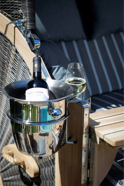 Eine Weinflasche in einem metallenen Eiskübel und ein gefülltes Weinglas stehen auf einer hölzernen Armlehne eines gestreiften Sitzpolsters.