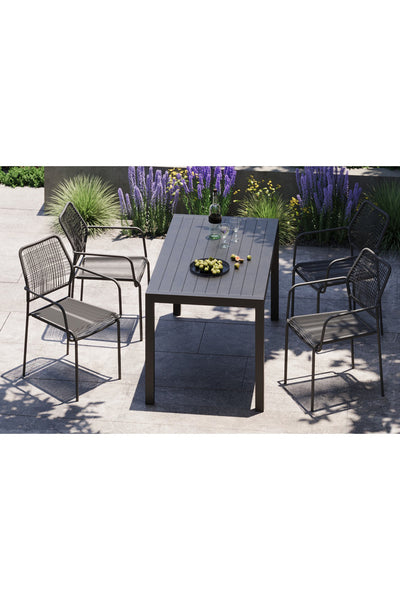 Ein rechteckiger Tisch im Freien mit vier Metallstühlen auf einer Terrasse, auf dem ein schwarzes Tablett mit Zitrusfrüchten steht, umgeben von lila blühenden Pflanzen.