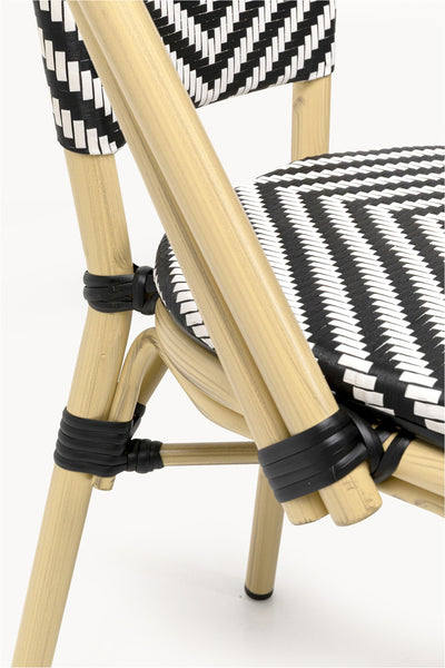 Nahaufnahme eines Stuhles mit hellem Holzgestell und schwarz-weiß geflochtener Sitzfläche und Rückenlehne in einem Chevron-Muster.