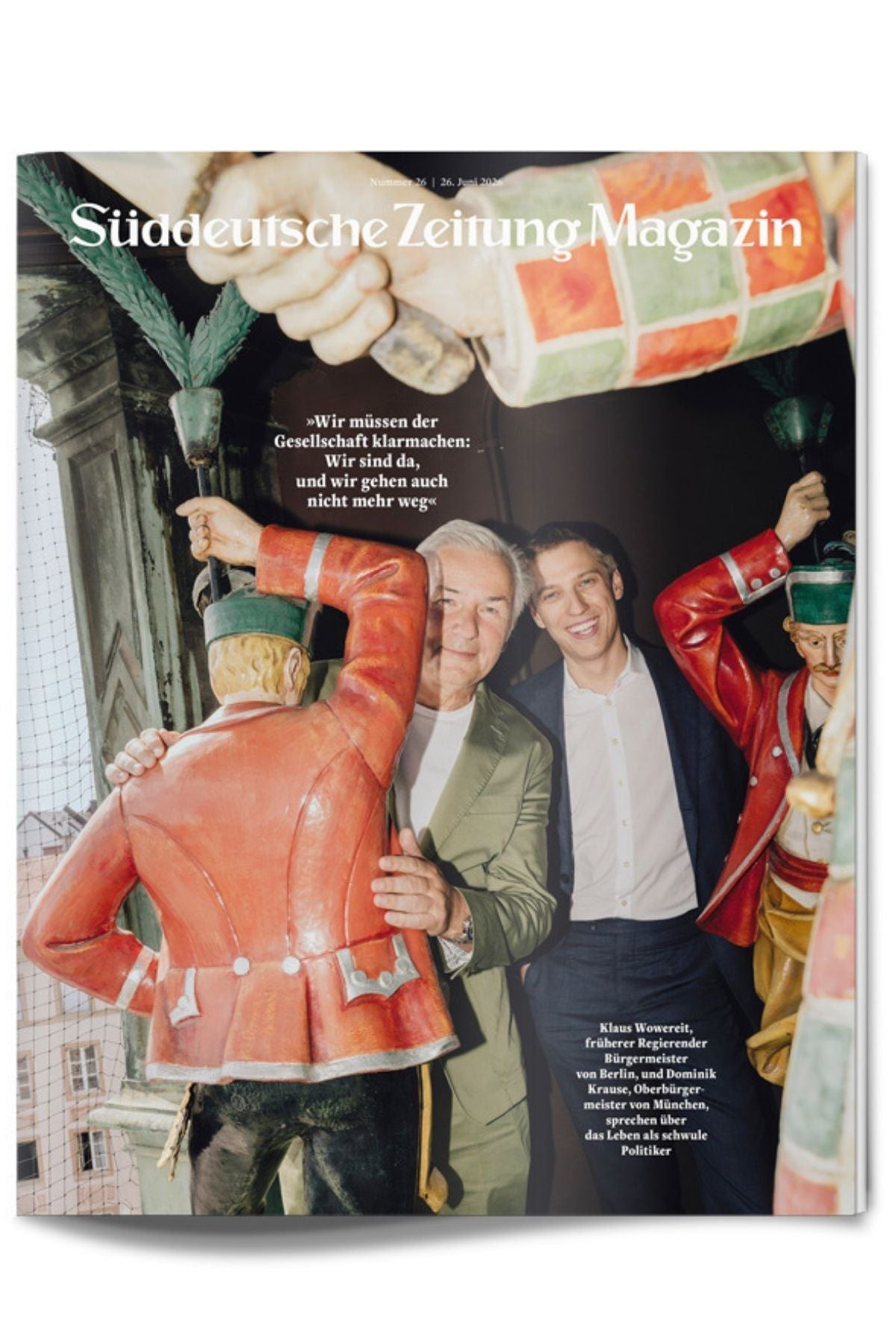Ein älterer Mann und ein jüngerer Mann stehen lächelnd zwischen zwei großen Holzsoldatenfiguren auf einem Balkon – so ist das Titelbild des „Süddeutschen Zeitungsmagazins“ gestaltet.