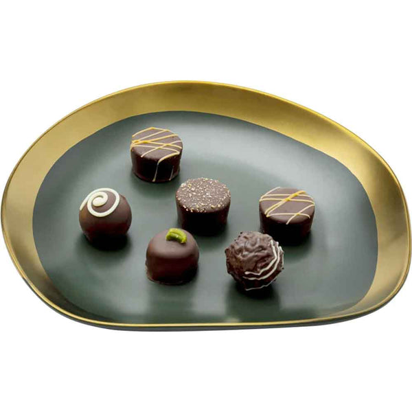 Sechs verschiedene Schokoladentrüffel auf einem eleganten, schwarzen Teller mit Goldrand.