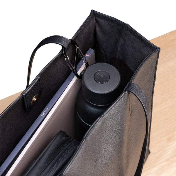 Eine schwarze Ledertasche mit einem Laptop, einer schwarzen Wasserflasche und einer Tasche mit Reißverschluss, die auf einer hölzernen Unterlage steht.