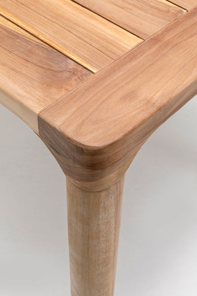 Nahaufnahme der Ecke eines Holztisches mit abgerundeten Kanten und glatter Oberfläche, die die Tischplatte und ein Bein vor einem schlichten Hintergrund zeigt.