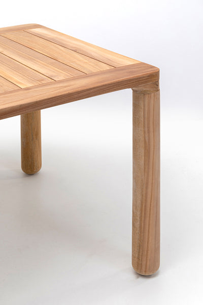 Nahaufnahme der Ecke eines Holztisches mit dicken, zylindrischen Beinen auf einem schlichten weißen Hintergrund.