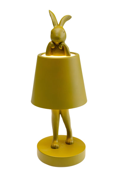 Gelbe Tischlampe in Form eines Kaninchens, wobei der Lampenschirm den Rumpf des Kaninchens bedeckt, so dass nur der Kopf und die Beine sichtbar sind.
