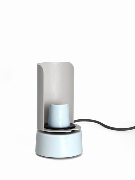 Ein moderner elektrischer Tassenwärmer aus Keramik mit einer hellblauen Tasse und einem schwarzen Stromkabel auf weißem Hintergrund.