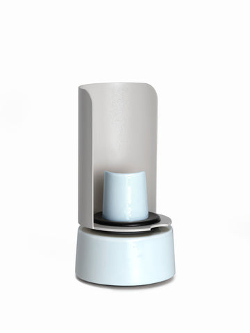 Minimalistische, moderne Lampe mit zylindrischem Lampenschirm und glänzend weißem Sockel, fotografiert vor einem weißen Hintergrund.