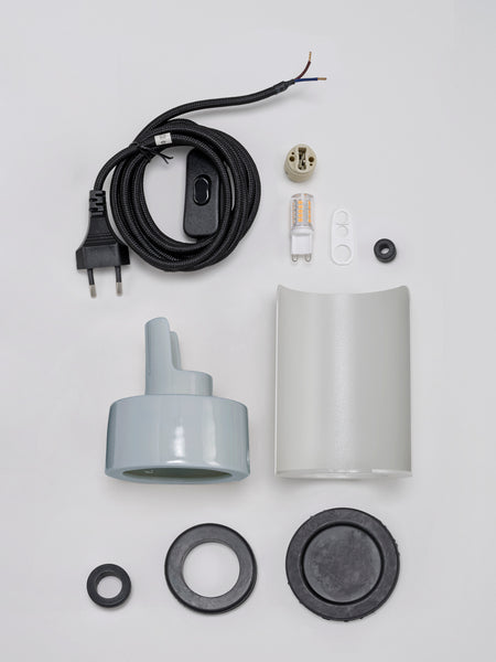 Lampenbausatz mit Kabel, Stecker, Glühbirne, Fassung, Schirm und verschiedenen Beschlagteilen, die auf einer weißen Fläche angeordnet sind.