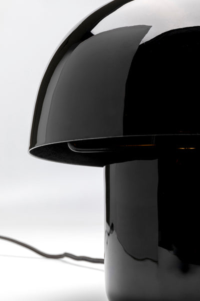 Nahaufnahme einer modernen schwarzen pilzförmigen Tischleuchte mit reflektierender Oberfläche und sichtbarem Kabel.