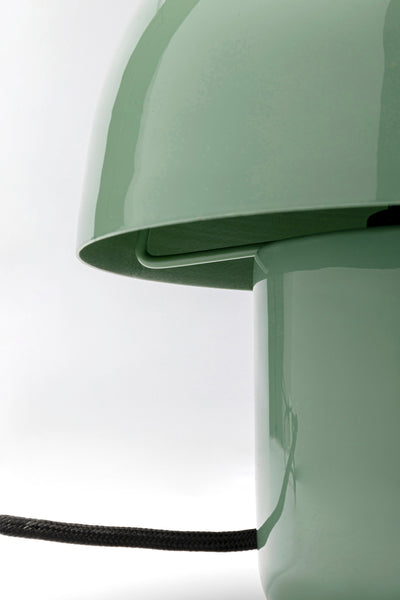 Nahaufnahme einer glänzenden, hellgrünen, kuppelförmigen Lampe mit schwarzem Netzkabel vor einem schlichten Hintergrund.