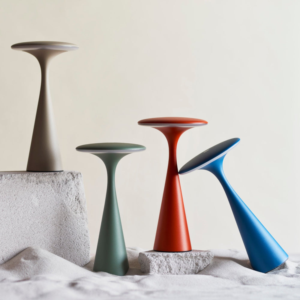 Vier moderne, pilzförmige Lampen in Beige, Grün, Rot und Blau sind auf strukturierten weißen Blöcken vor einem neutralen Hintergrund angeordnet.