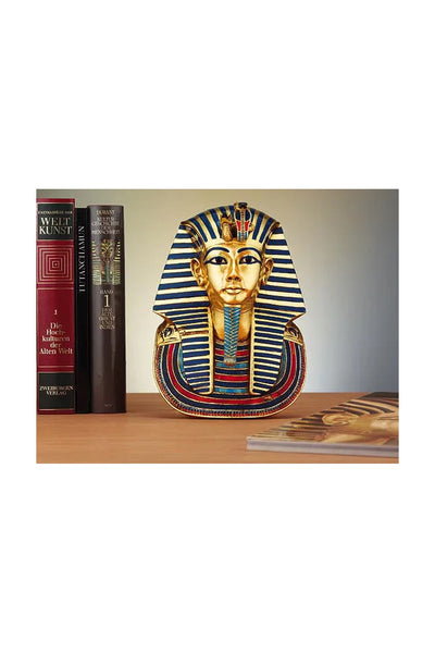 Eine kleine Nachbildung der Maske von König Tutanchamun liegt auf einer Holzfläche zwischen Büchern über Weltkunst und alte Geschichte.