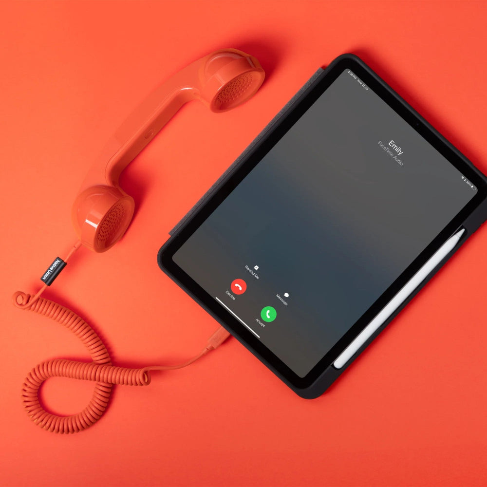 Ein orangefarbener Retro-Telefonhörer, der an ein Tablet mit einem Bildschirm für eingehende Anrufe angeschlossen ist, auf einem passenden orangefarbenen Hintergrund.