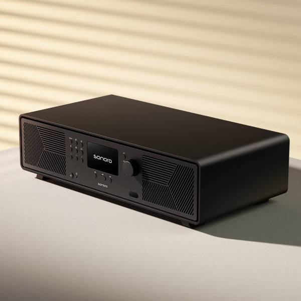 Ein schwarzes Sonoro-Audiogerät mit Tasten und einem Display, das auf einer hellen Fläche mit gestreiften Schatten steht.