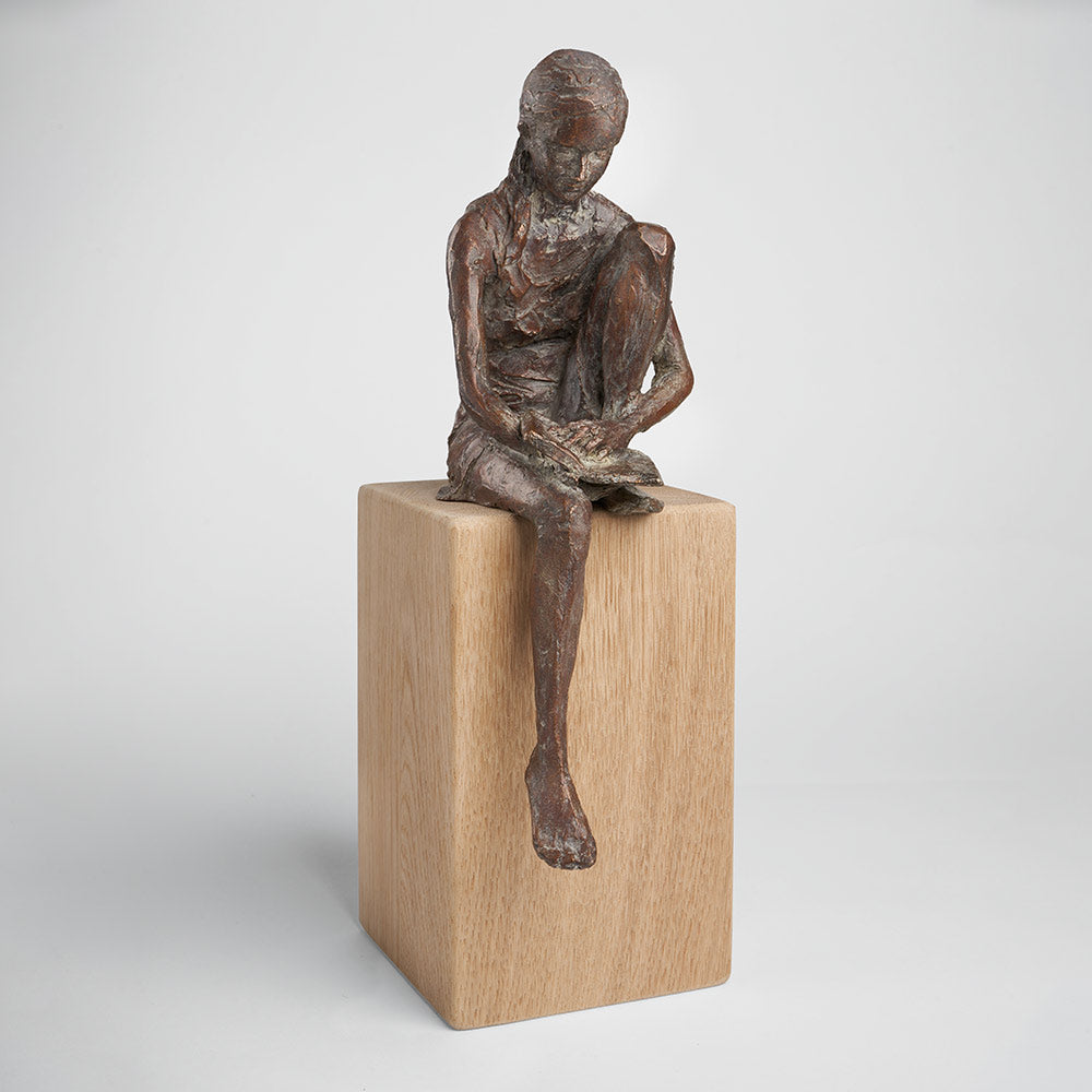 „Lesende“ von Valerie Otte ist eine Bronzeskulptur eines lesenden Mädchens auf einem Eichensockel, mit einem erhobenen Bein.