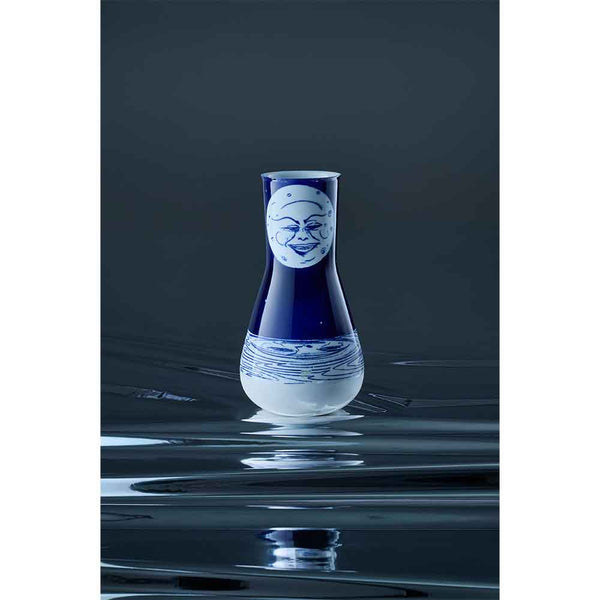 Eine blau-weiße Vase mit einem lächelnden Gesicht vor einem dunklen, reflektierenden Hintergrund.