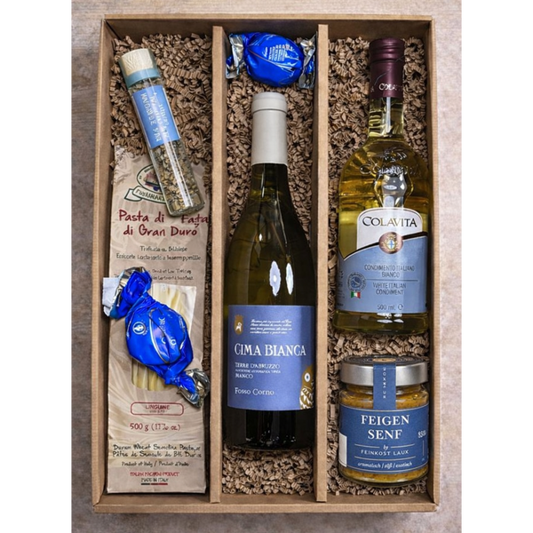 Eine Geschenkbox mit Nudeln, Weißwein, Olivenöl, Senf, Kräutern und zwei verpackten Pralinen.