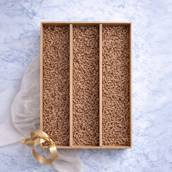 Eine rechteckige Schachtel mit drei Abschnitten, gefüllt mit braunem Reis und einem goldenen Band auf hellblauem Grund.
