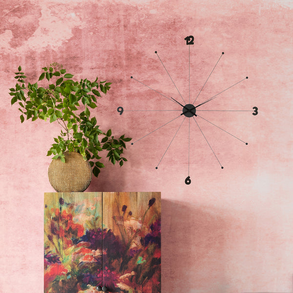 Eine minimalistische Wanduhr an einer rosafarbenen Wand über einem Schrank mit Pflanzen- und Blumendekor.