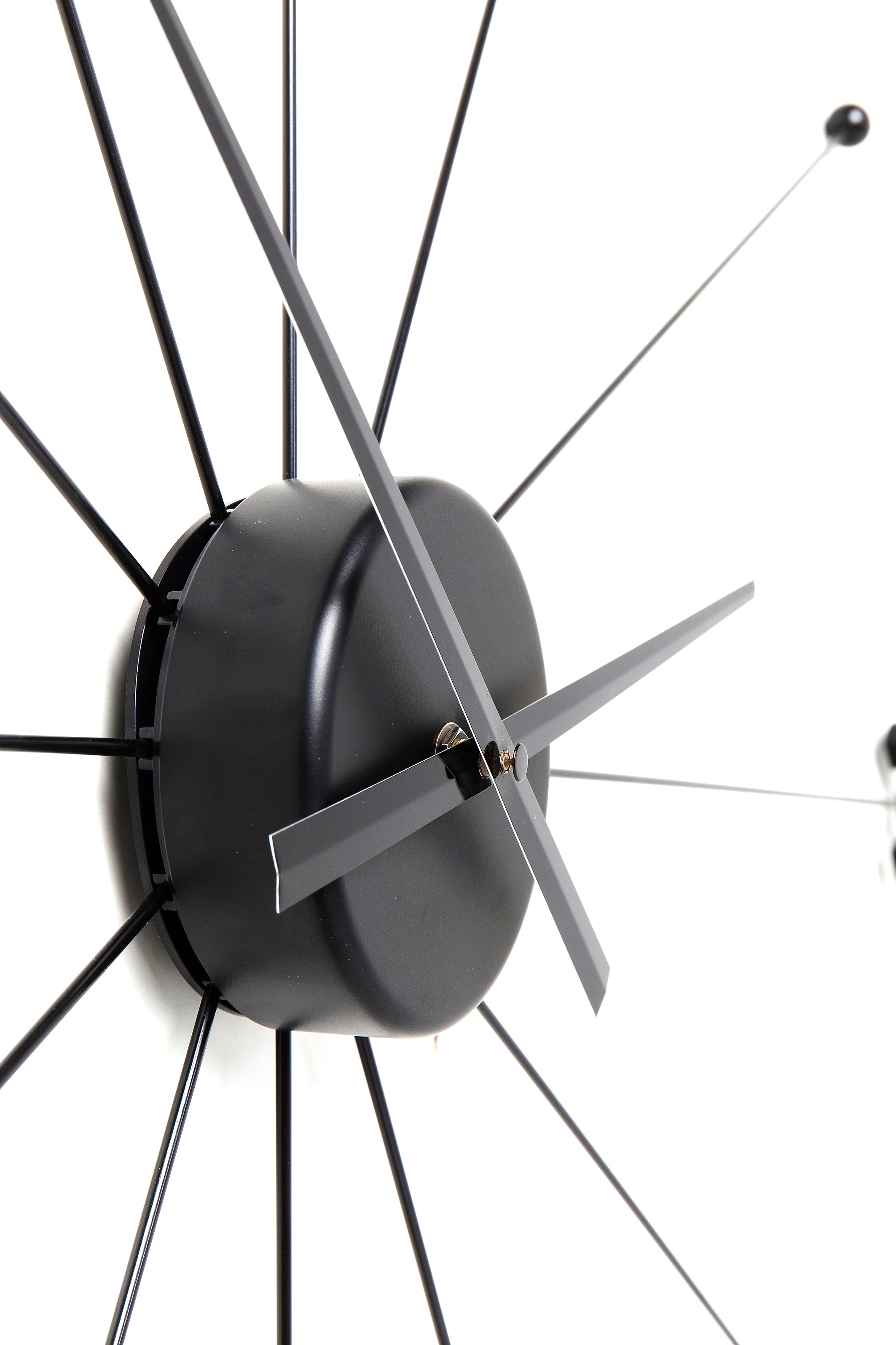 Nahaufnahme einer modernen schwarzen Wanduhr mit minimalistischen Zeigern und strahlenden Speichen auf weißem Hintergrund.
