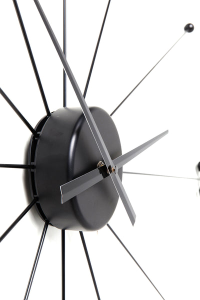 Nahaufnahme einer modernen schwarzen Wanduhr mit minimalistischen Zeigern und strahlenden Speichen auf weißem Hintergrund.