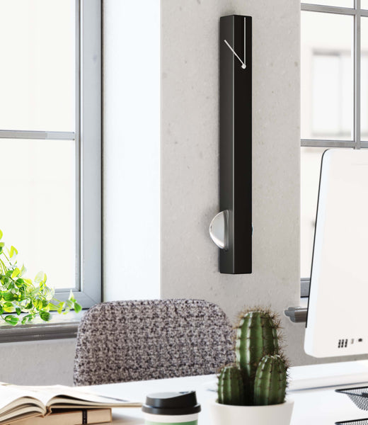 Eine moderne schwarze Wanduhr mit Zeigern, montiert an einer weißen Wand in einem hellen Büroraum.